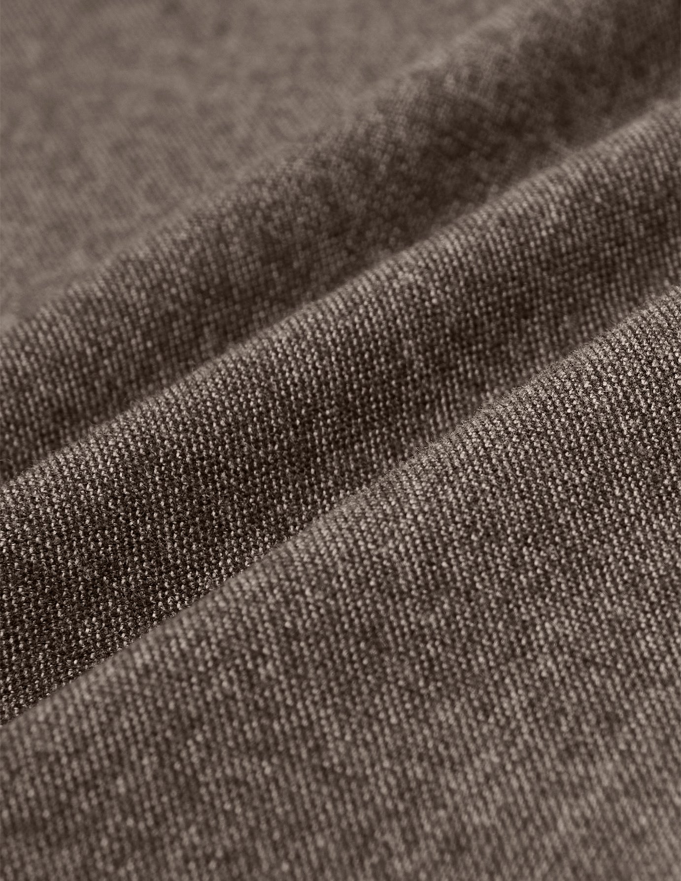 Nærbilde av de brune Atelier Pants Relaxed Dark Beige i brutt twill-stoff med synlig veving og diagonale folder.